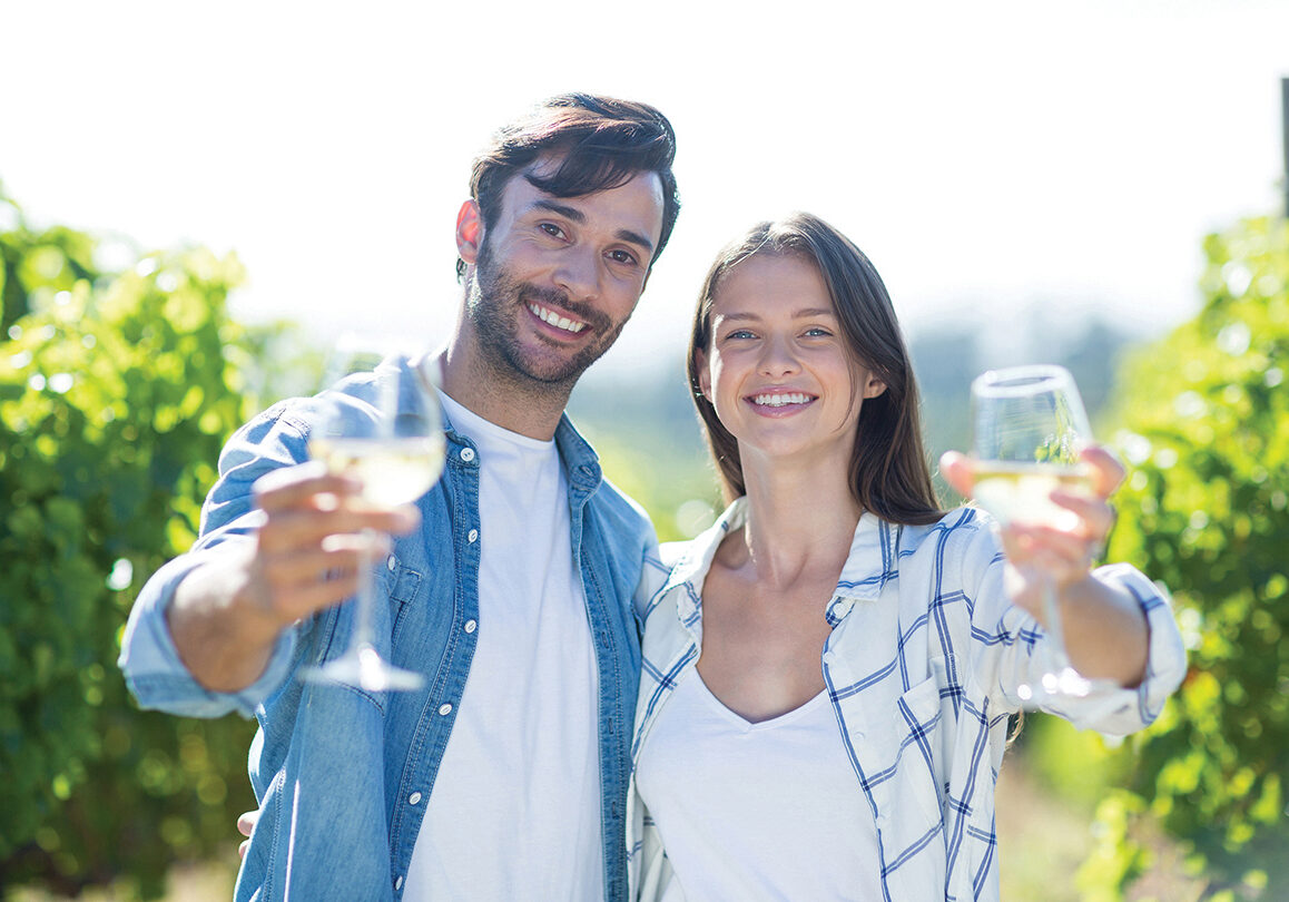 Portrait of smiling couple showing wineglasses standing at vineyard