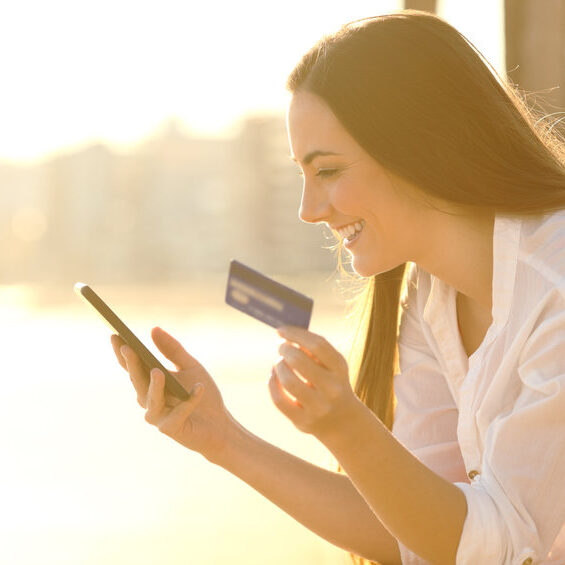 Side view portrait of a happy woman paying online with credit card and smart phone at sunset